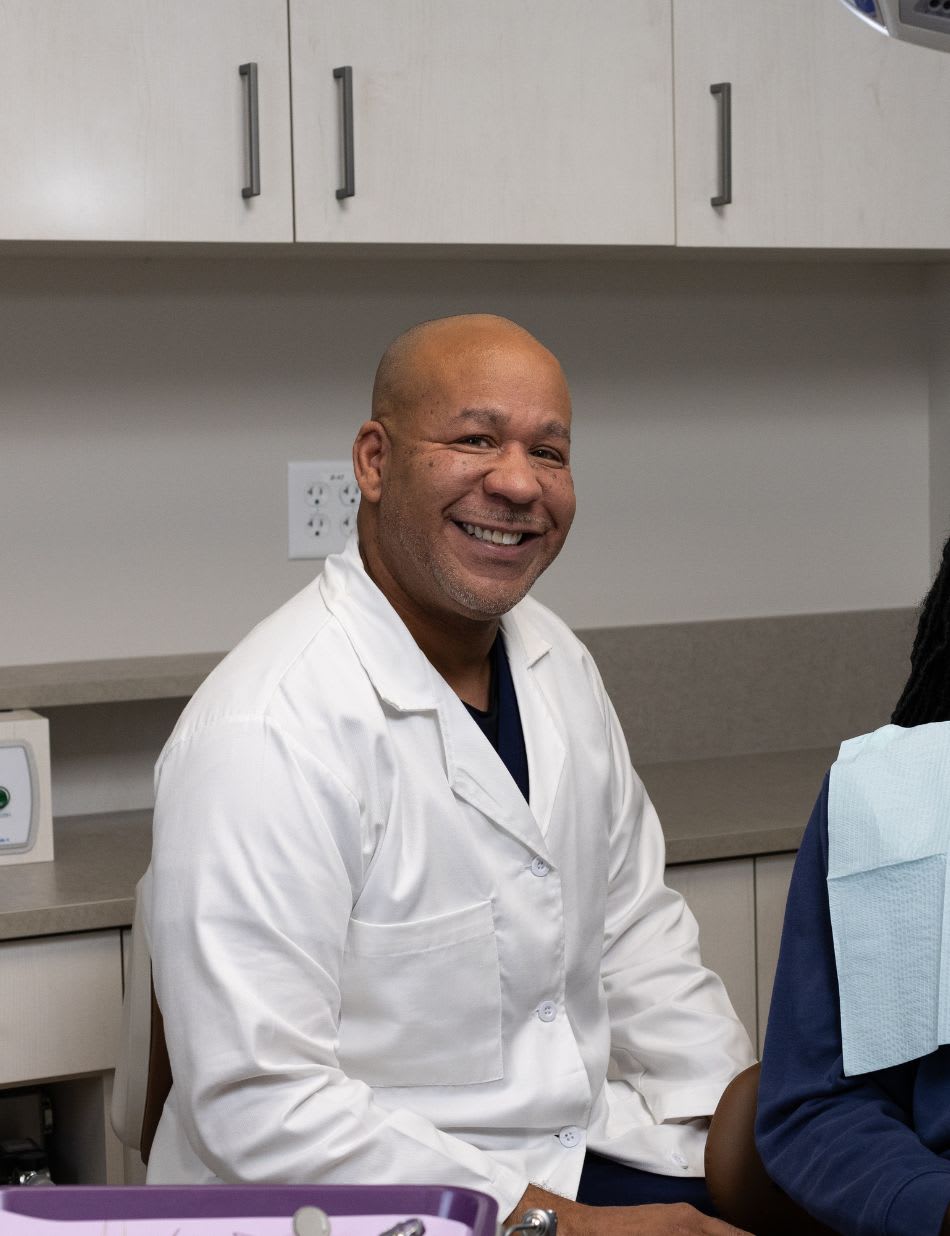 A smiling dentist seated in an exam room