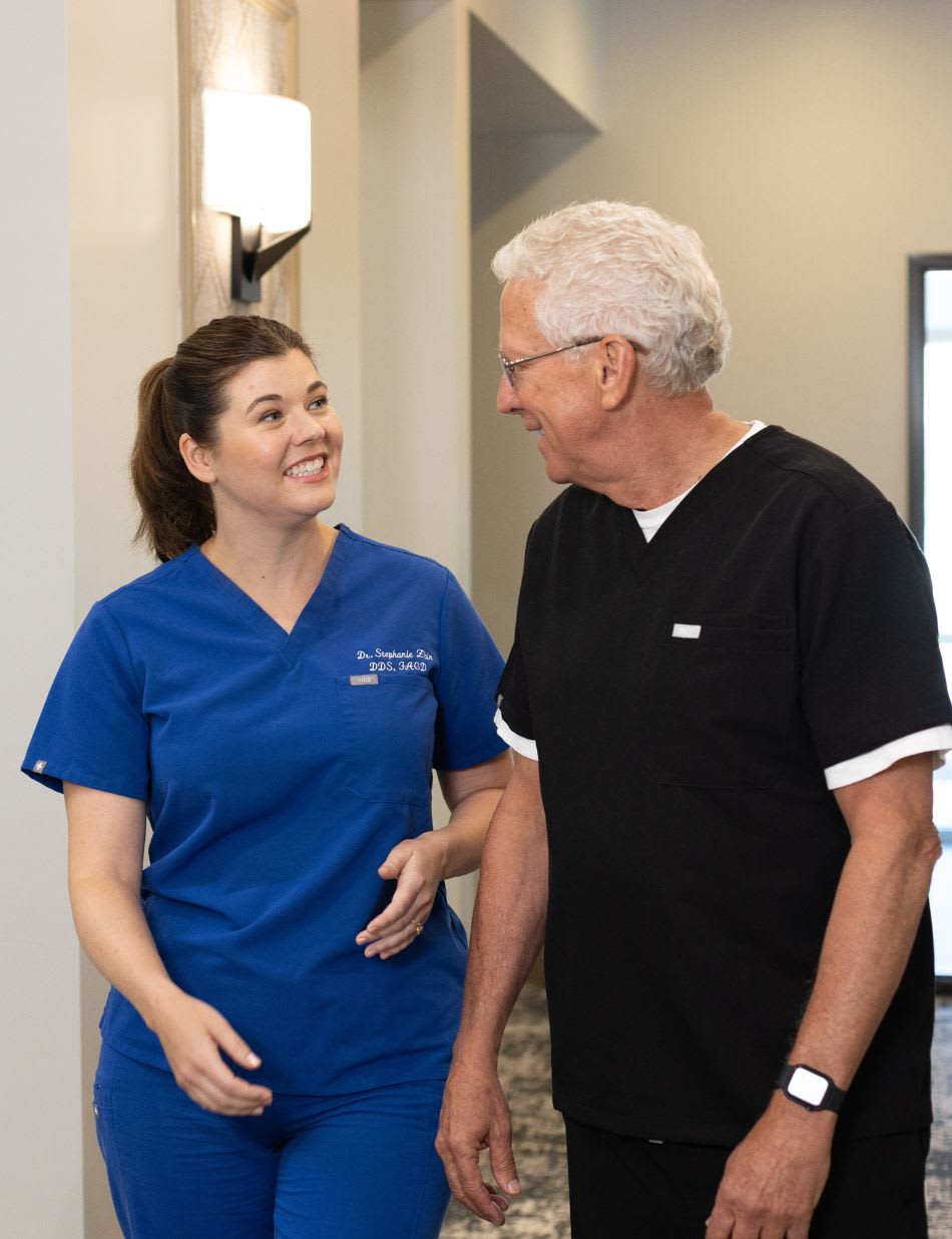A dental team member in blue scrubs laughing with a colleague