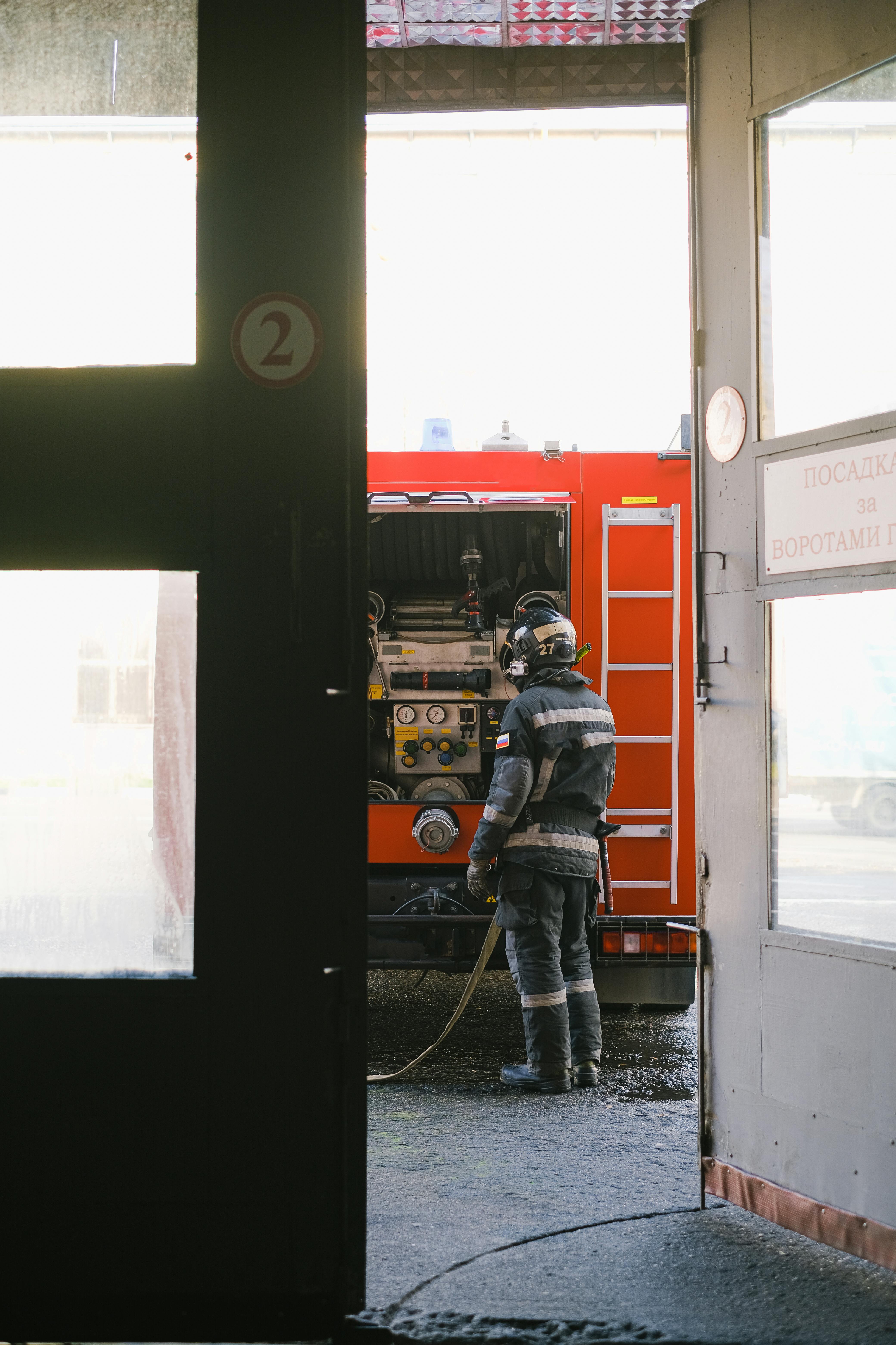 Firefighter in full gear stands by a fire truck, ready for action outside a building.