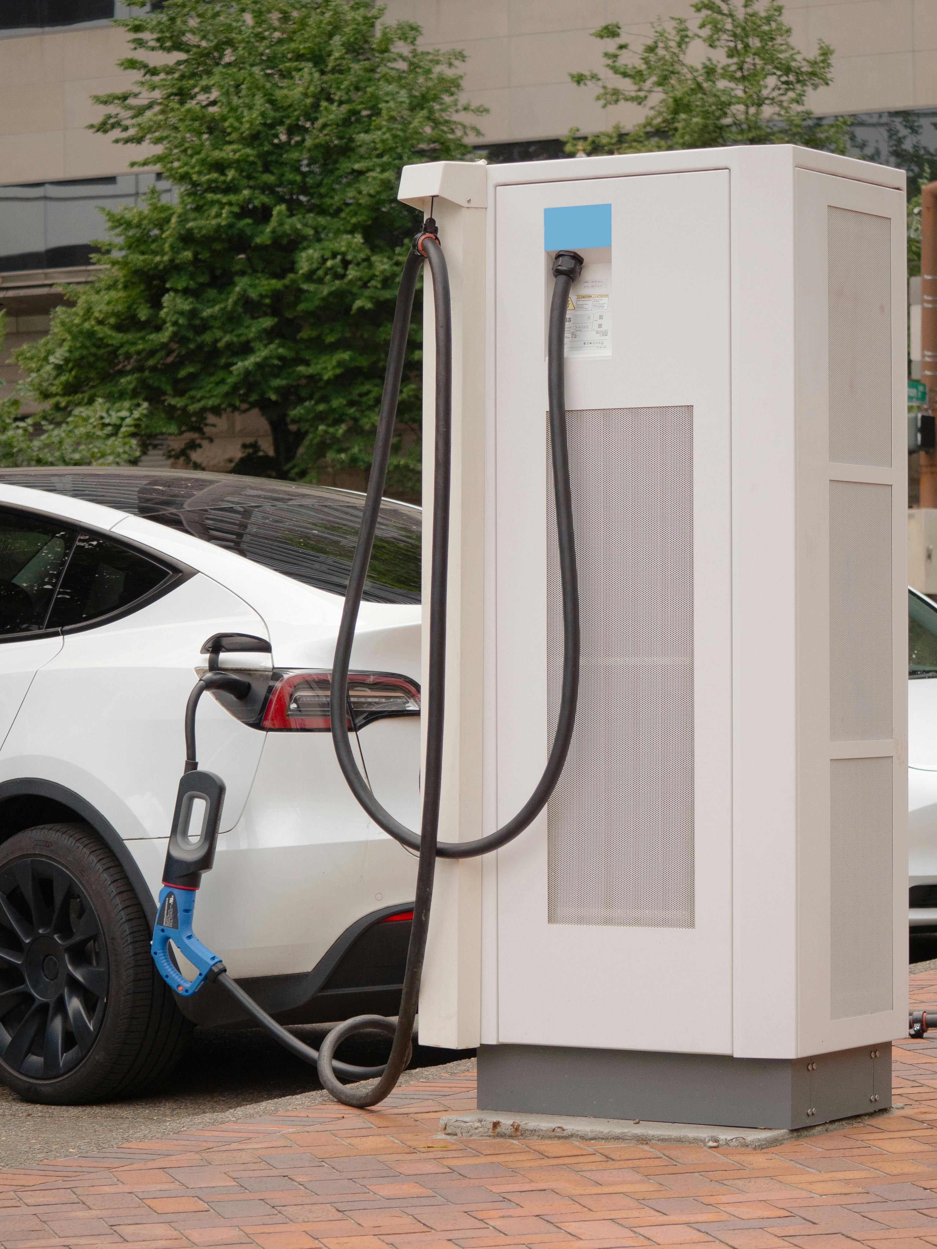 A white electric car plugged into a charging station in a city setting, showcasing sustainable energy.