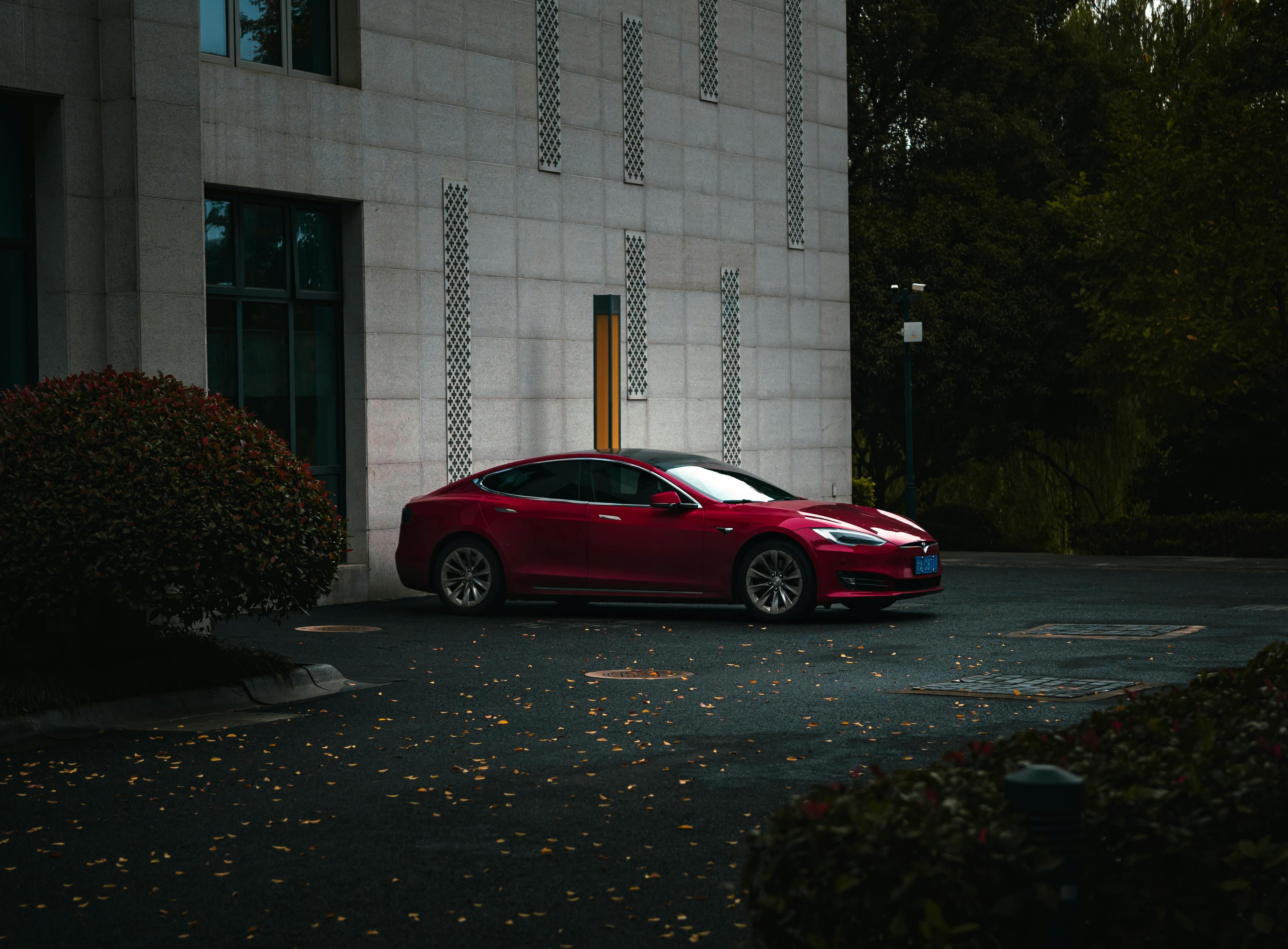 A sleek red electric car parked beside a modern building in an urban environment.