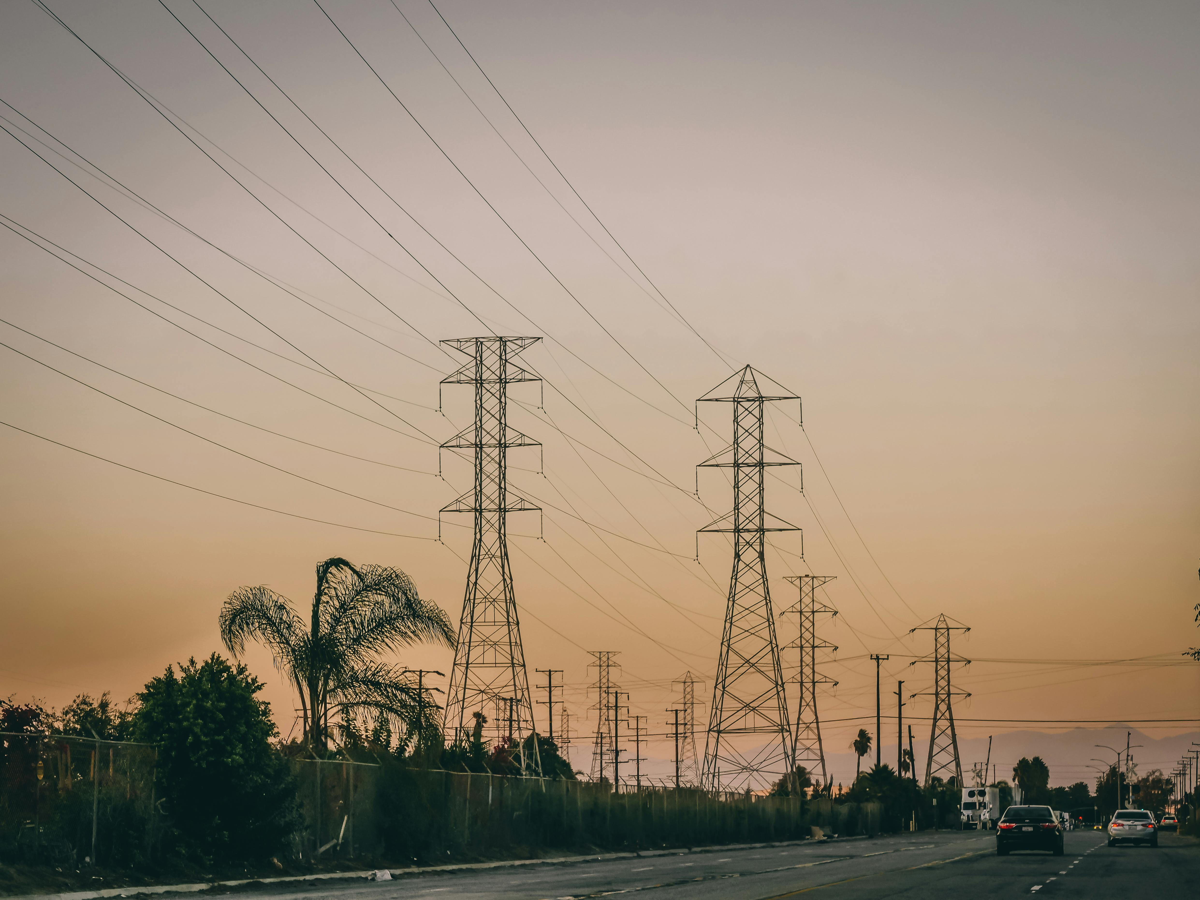 Transmission towers and road under a sunset sky symbolizing energy distribution.