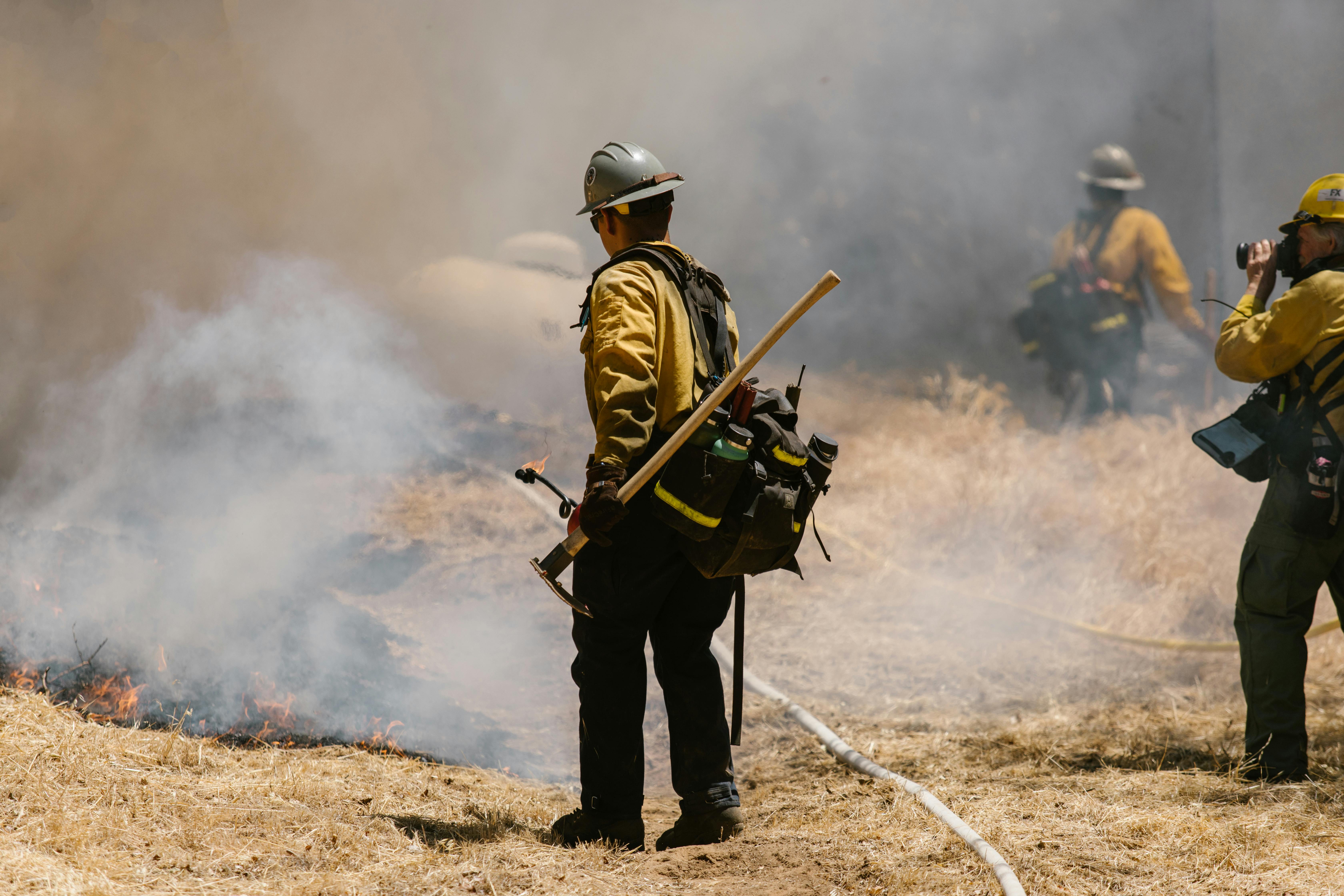 Firefighters in action combating a forest fire with smoke and flames visible.