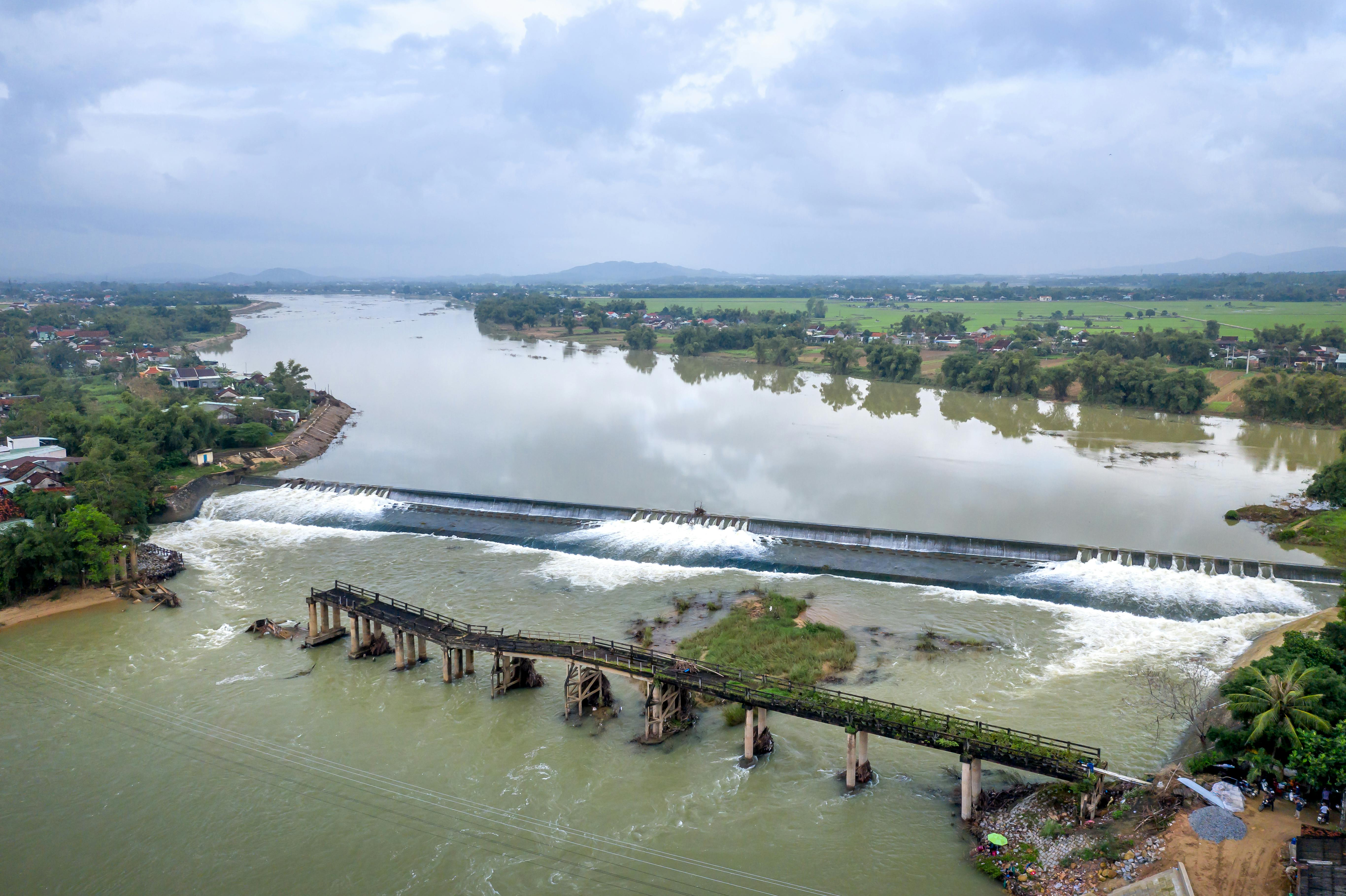 Scenic aerial view of a river with a dam and an old wooden bridge surrounded by farmland.