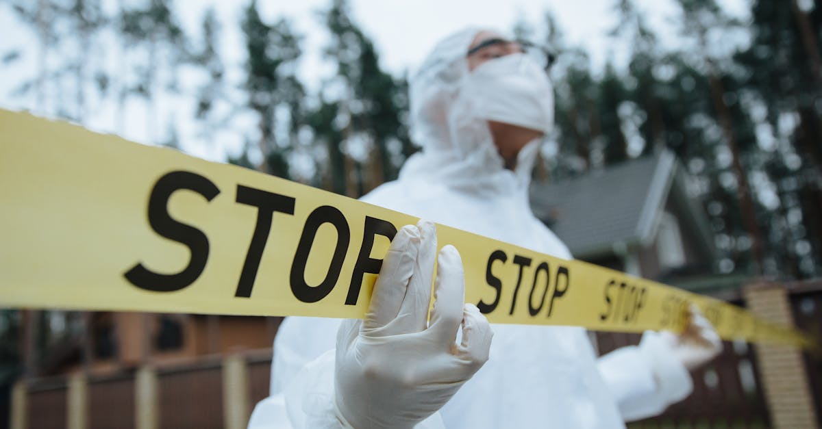 Investigator in protective gear securing crime scene with stop tape outdoors.