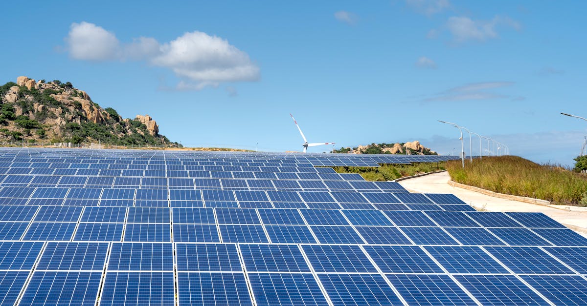 Expansive solar farm with rows of panels under clear blue sky and hills in the background.