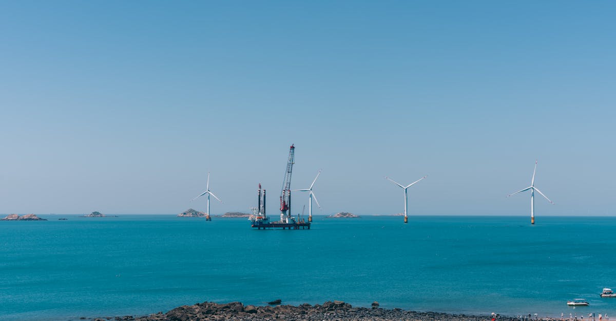 A serene view of offshore wind turbines against a clear blue sky with calm ocean waters.