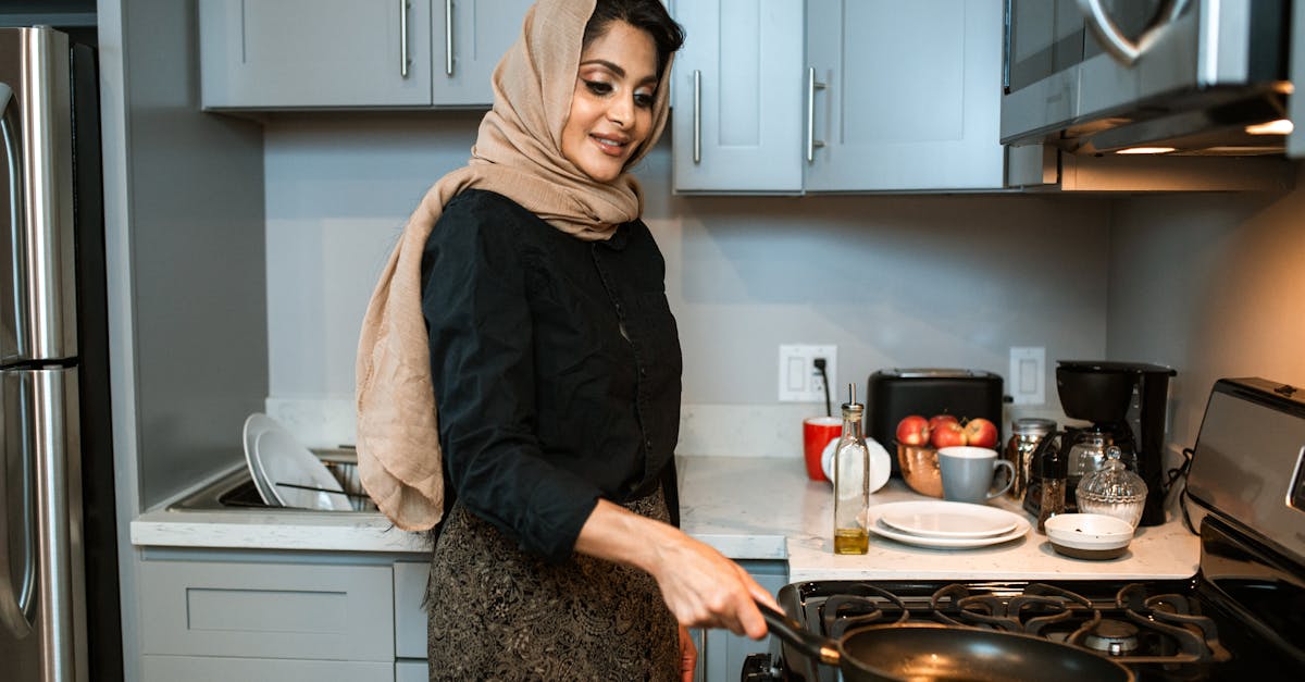 A cheerful woman wearing a headscarf cooks a meal in a contemporary kitchen.