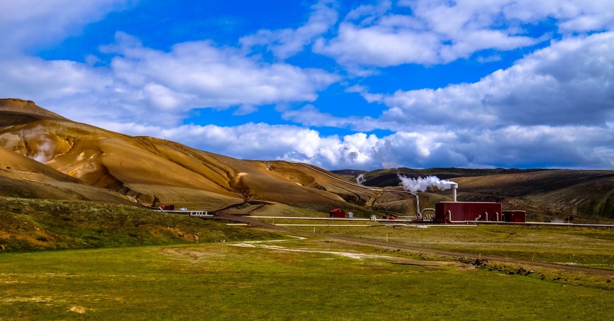 Beautiful countryside landscape with a factory and smoke against a backdrop of rolling hills and blue sky.