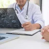 Doctor reviewing brain MRI scans and taking notes during patient consultation.&nbsp;