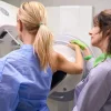 Radiographer positioning a patient for mammography breast imaging in a hospital radiology room.&nbsp;