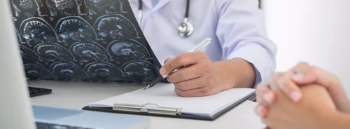 Doctor reviewing brain MRI scans and taking notes during patient consultation.&nbsp;