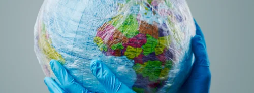 Global health protection concept with gloved hands holding a plastic-wrapped Earth.