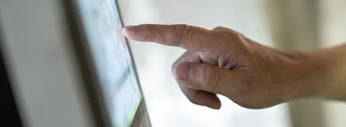 Close-up hand tapping a touchscreen kiosk, finger pressing digital interface.&nbsp;