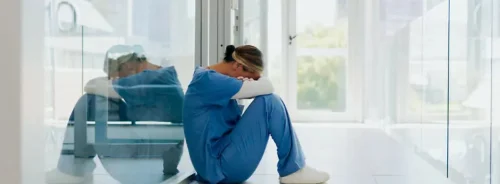 Healthcare worker burnout concept with exhausted clinician sitting alone in hospital corridor.&nbsp;