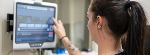 Healthcare professional accessing or updating patient data on a digital touchscreen system in a clinical environment.&nbsp;