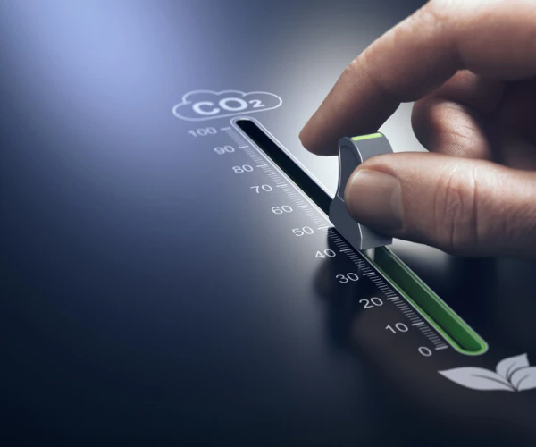 Hand adjusting a control knob to reduce CO₂ emissions,&nbsp;representing&nbsp;environmental sustainability, carbon footprint reduction, and green innovation efforts.&nbsp;