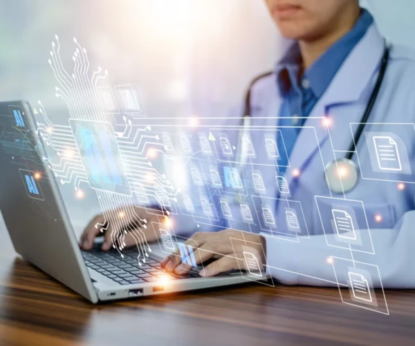 Clinician working on a laptop with an AI-driven document and data interface overlay.&nbsp;