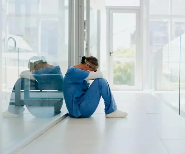 Healthcare worker burnout concept with exhausted clinician sitting alone in hospital corridor.&nbsp;