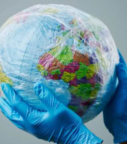 Global health protection concept with gloved hands holding a plastic-wrapped Earth.