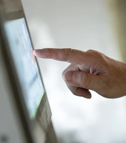 Close-up hand tapping a touchscreen kiosk, finger pressing digital interface.&nbsp;