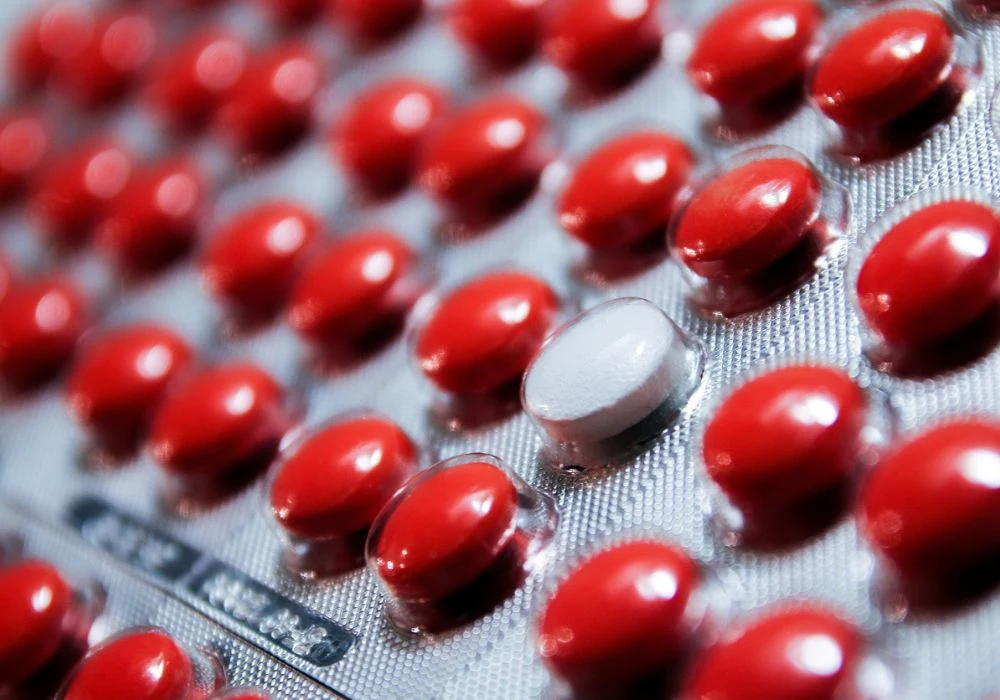 Close-up of red tablets in blister pack with one white pill standing out, symbolising uniqueness or medication variation&nbsp;