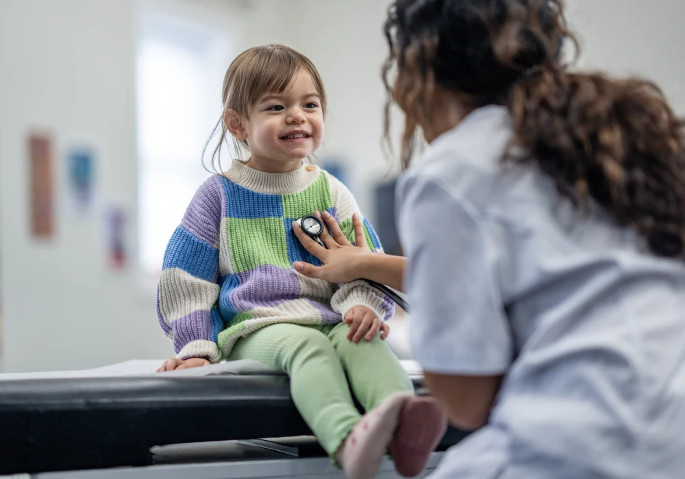 Paediatric check-up &ndash; smiling child with doctor using stethoscope during routine health exam&nbsp;