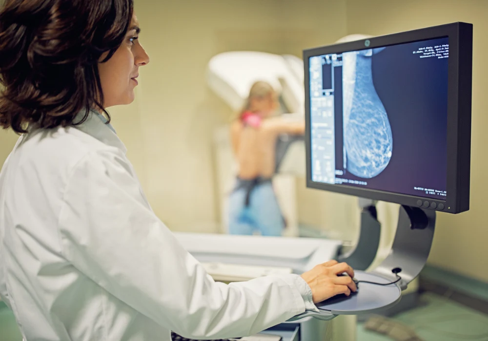 Radiologist reviewing digital mammogram while patient undergoes breast imaging, highlighting early detection and diagnosis of breast cancer through advanced radiology systems.&nbsp;