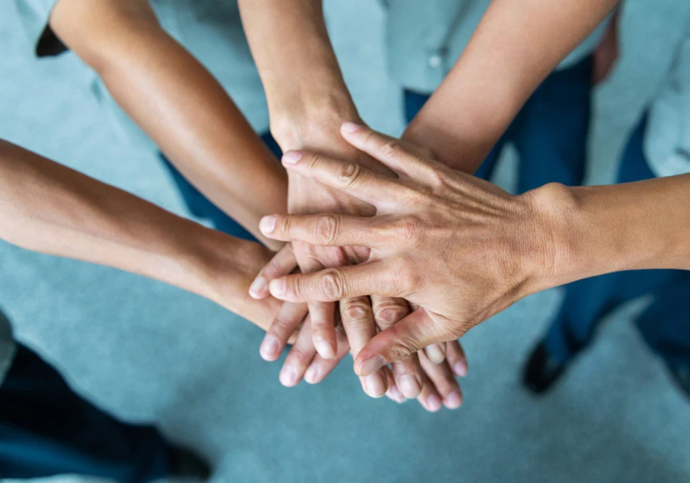 Team members joining hands to symbolise collaboration, trust and unity in a workplace setting