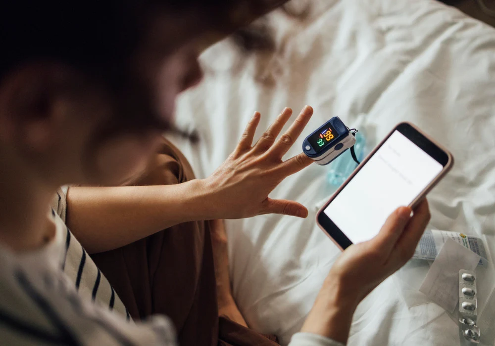 Woman uses pulse oximeter and smartphone for remote health monitoring at home.&nbsp;