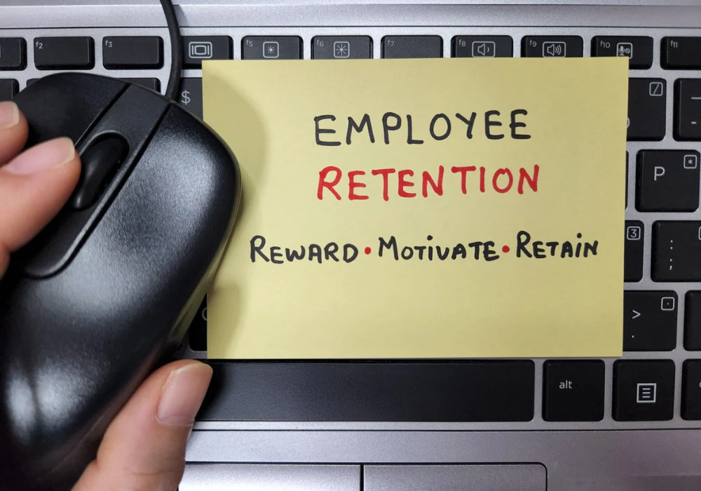 Employee retention strategy message on sticky note over laptop keyboard, highlighting reward, motivation and retention goals.&nbsp;