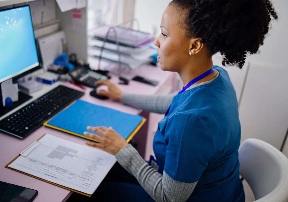 Female healthcare professional updating electronic medical records at a clinic workstation.