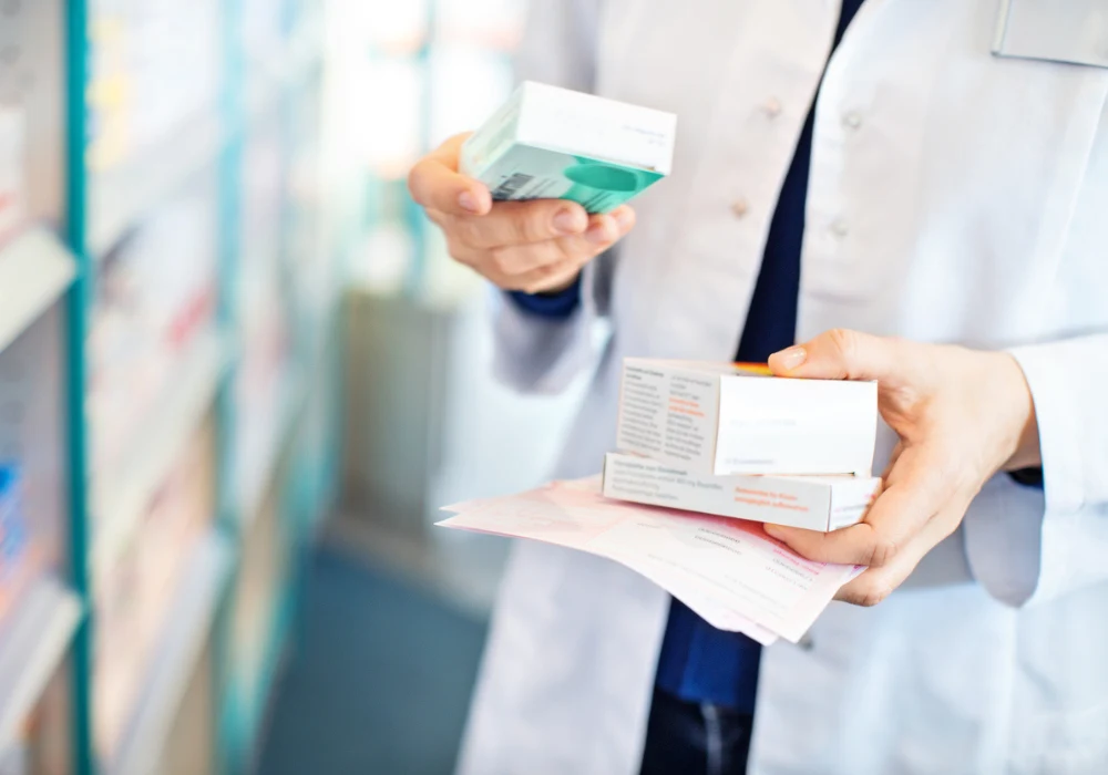 Pharmacist reviewing prescription medication boxes and patient instructions in a pharmacy setting.&nbsp;