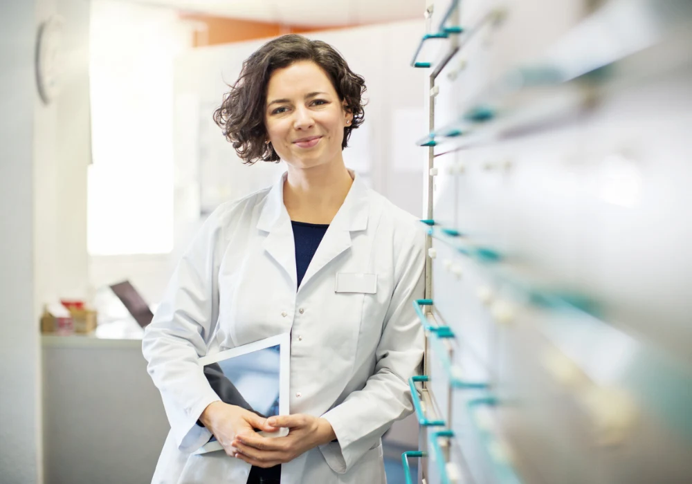 Confident female pharmacist in white coat holding a digital tablet in a modern pharmacy.&nbsp;