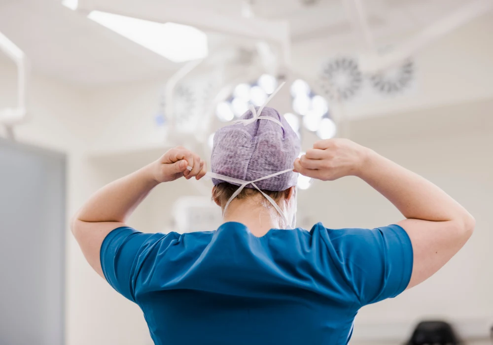 Surgeon preparing for operation: medical professional ties surgical cap in operating theatre.&nbsp;