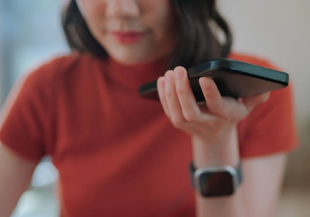 Woman using voice assistant on smartphone at home, close-up interaction.&nbsp;