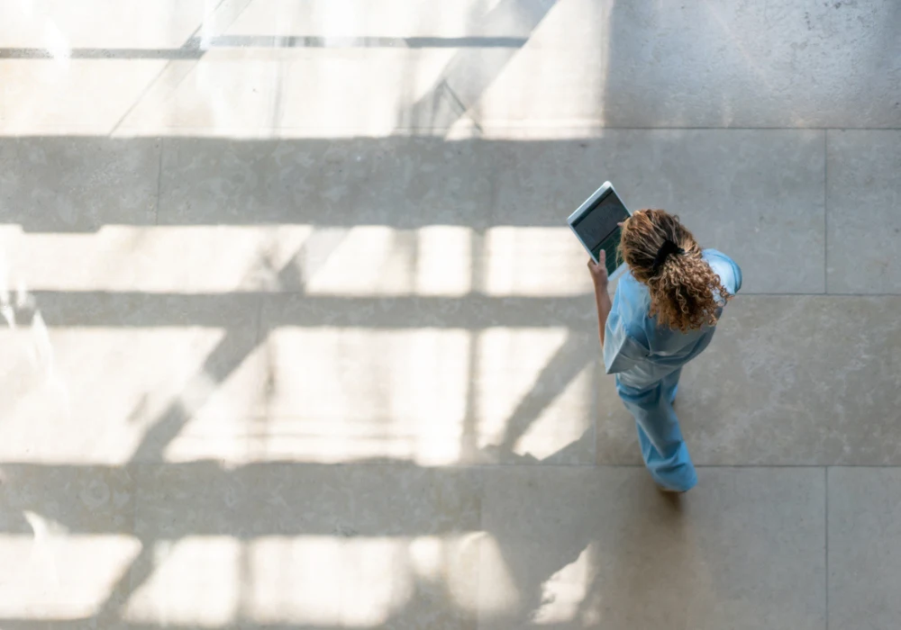 Overhead view of female healthcare worker walking in hospital corridor with digital tablet&nbsp;