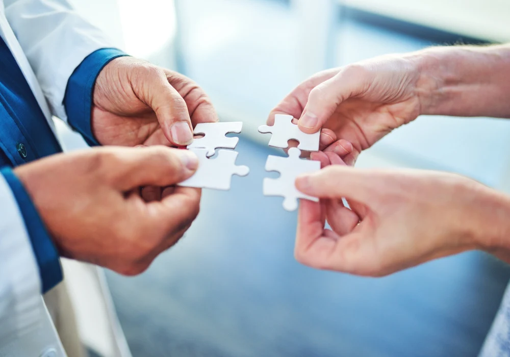 Close-up of hands holding puzzle pieces symbolising teamwork and collaboration in healthcare&nbsp;