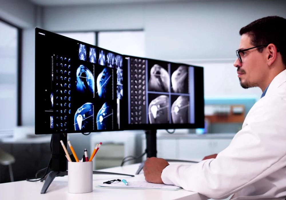 Radiologist examining digital MRI scans on dual monitors for advanced medical imaging analysis.&nbsp;