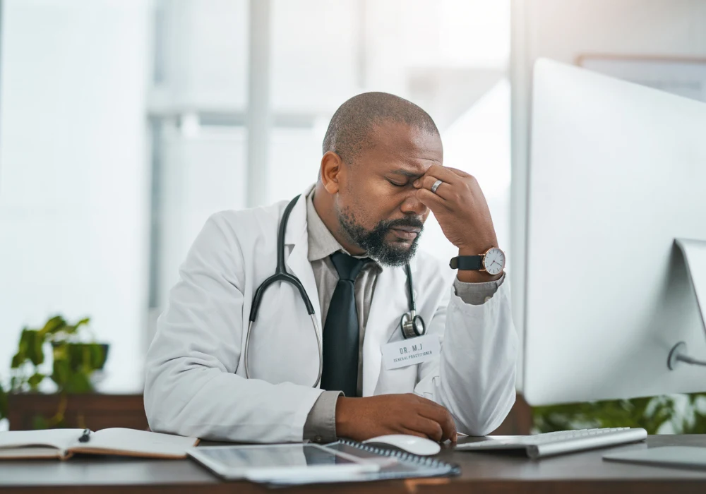 Stressed clinician at computer illustrating healthcare burnout from digital workload.&nbsp;
