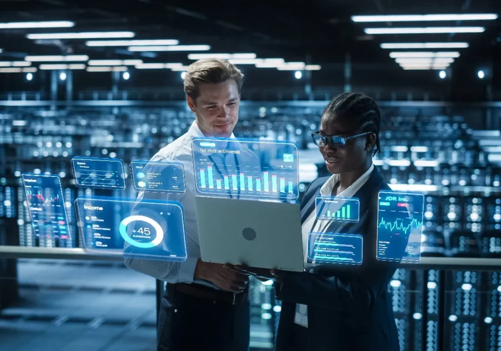 Data centre engineers analysing AI dashboards on a laptop in a server room.&nbsp;