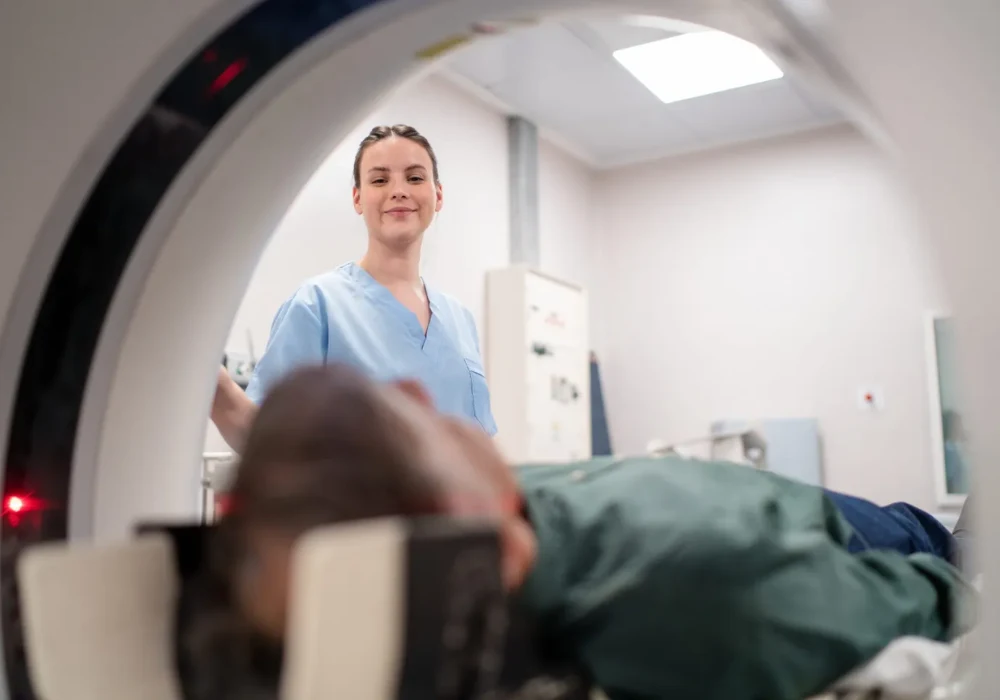 Radiology technologist preparing patient for CT scan inside hospital imaging suite.