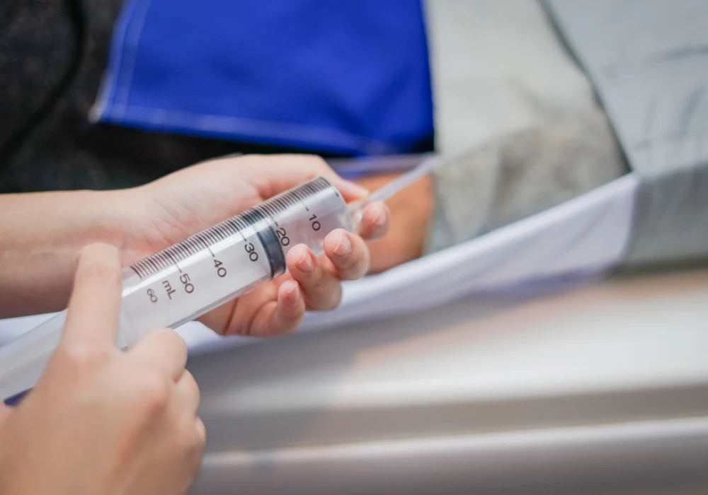 Healthcare worker holding a large syringe connected to a feeding or suction tube.&nbsp;