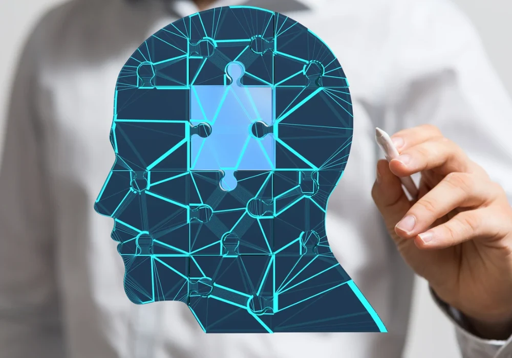 A digital illustration of a human head filled with interconnected neural network nodes,&nbsp;symbolising&nbsp;artificial intelligence, with a person holding a stylus in the background.&nbsp;