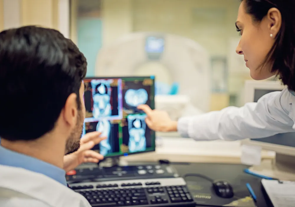 Radiologists analysing CT scan images at a workstation near a CT scanner to support diagnostic accuracy and patient care decisions.
