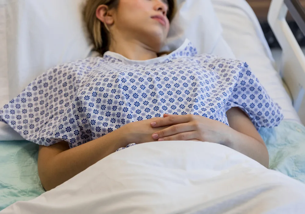 Young female patient resting in hospital bed wearing a medical gown after surgery or treatment.&nbsp;