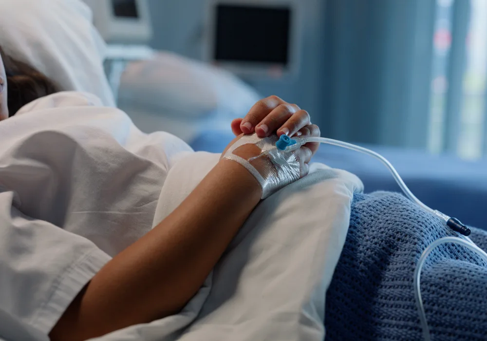 Hospital patient lying in bed with IV drip catheter in hand receiving medical treatment.&nbsp;