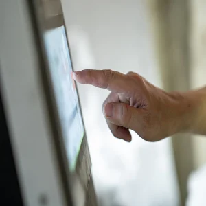 Close-up hand tapping a touchscreen kiosk, finger pressing digital interface.&nbsp;
