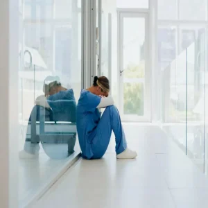 Healthcare worker burnout concept with exhausted clinician sitting alone in hospital corridor.&nbsp;