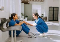 Compassionate support between healthcare workers in a hospital corridor, highlighting emotional resilience, teamwork, and mental health awareness in clinical environments.&nbsp;